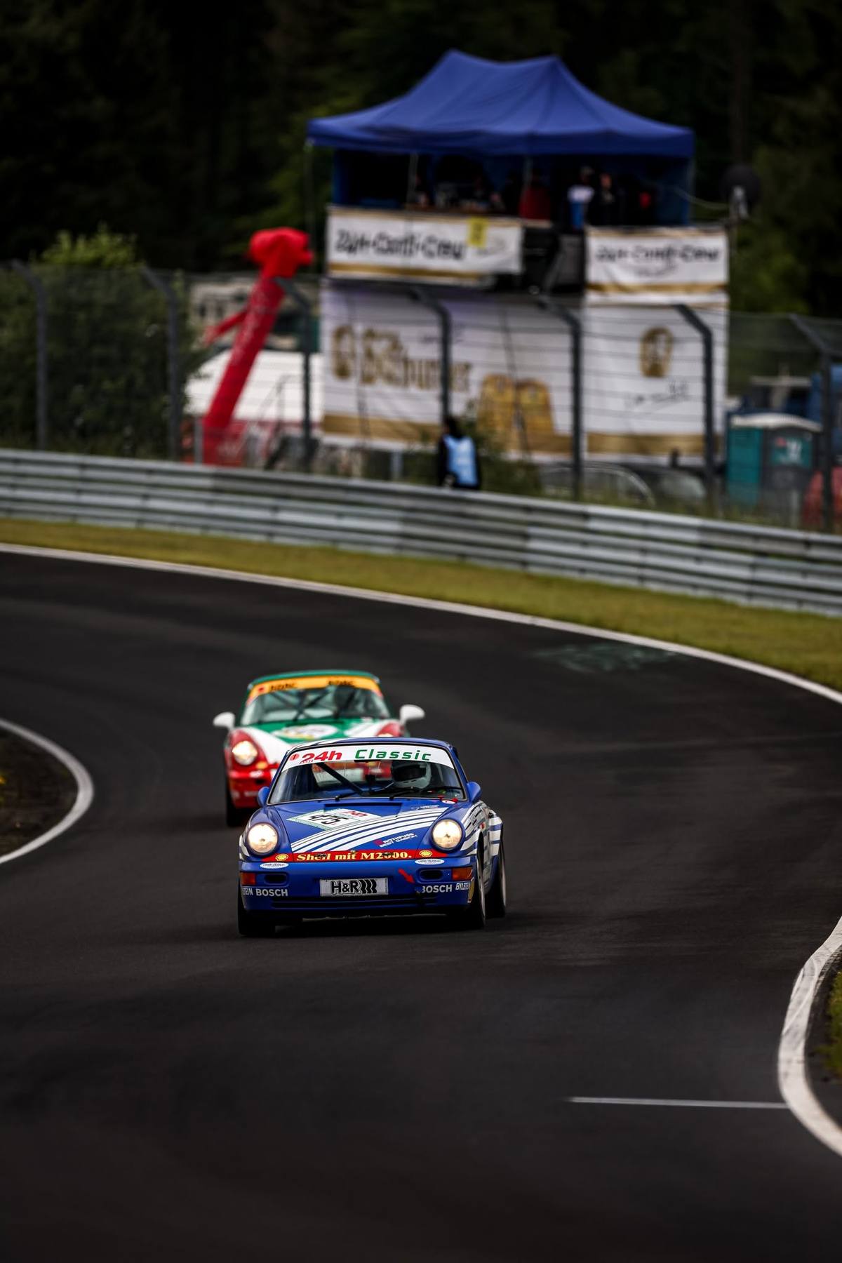 Der blaue Aimpoint-Porsche 964 mit Startnummer 52 in einer Kurve der Nordschleife, dahinter ein Mitbewerber, beim ADAC 24h Classic